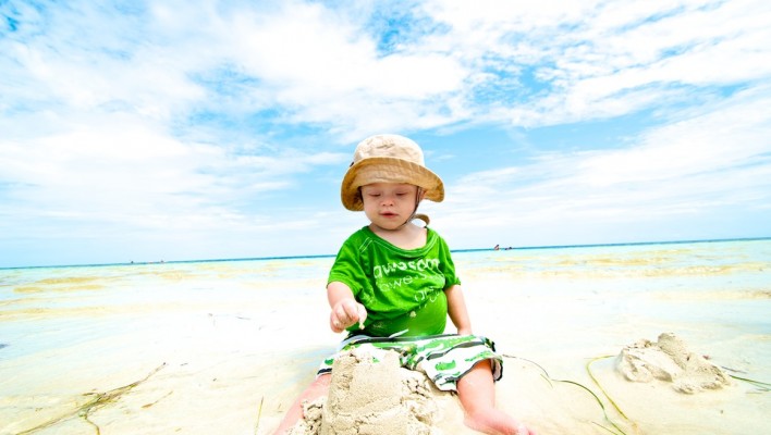 baby with Down syndrome building with sandcaslte on beach