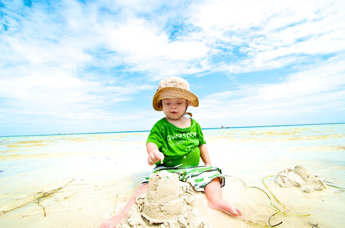 baby with Down syndrome building with sandcaslte on beach